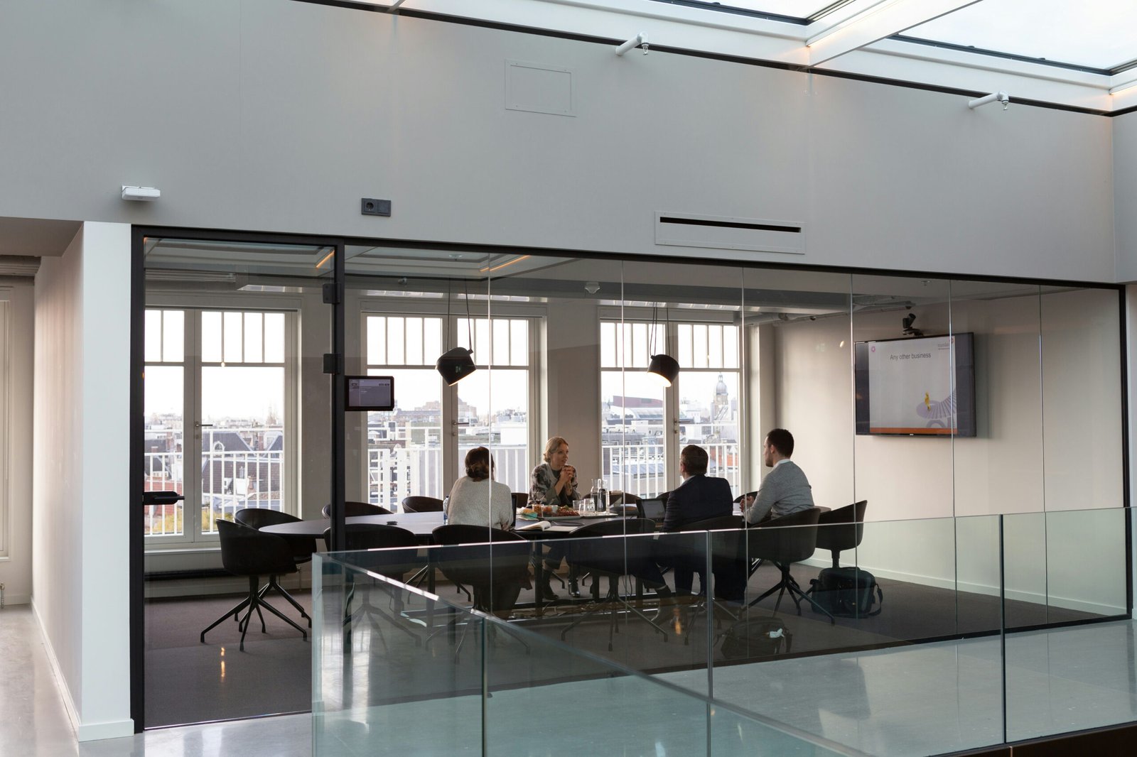 A small team meeting around a table in a glass-walled meeting room overlooking the city.